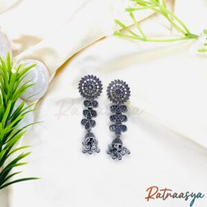 Elegant oxidized silver floral jhumka earrings with intricate design on white fabric background