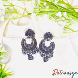 Peacock motif crescent oxidized earrings by Ratnaasya with ornate details and sparkling danglers on a cream background