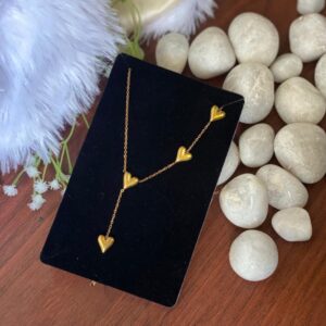 Gold heart pendant necklace on black velvet with white pebbles and fur​